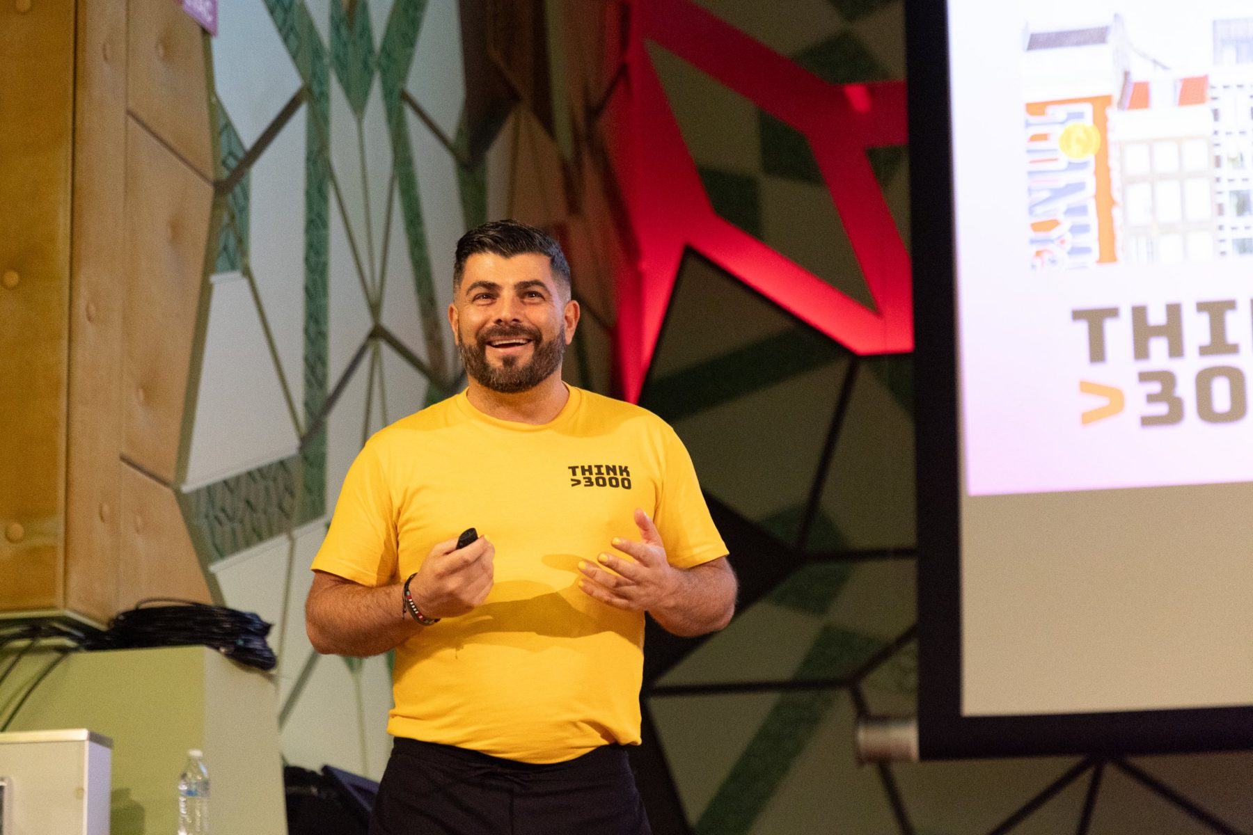 Kyriakos Gold presenting on stage, smiling, slide clicker in hand